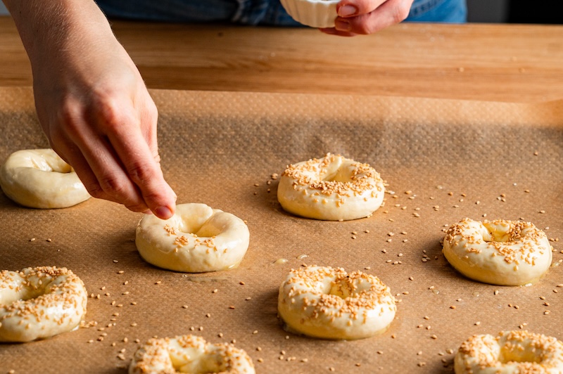 Rohe Bagels auf einem Blech werden mit Sesam bestreut.