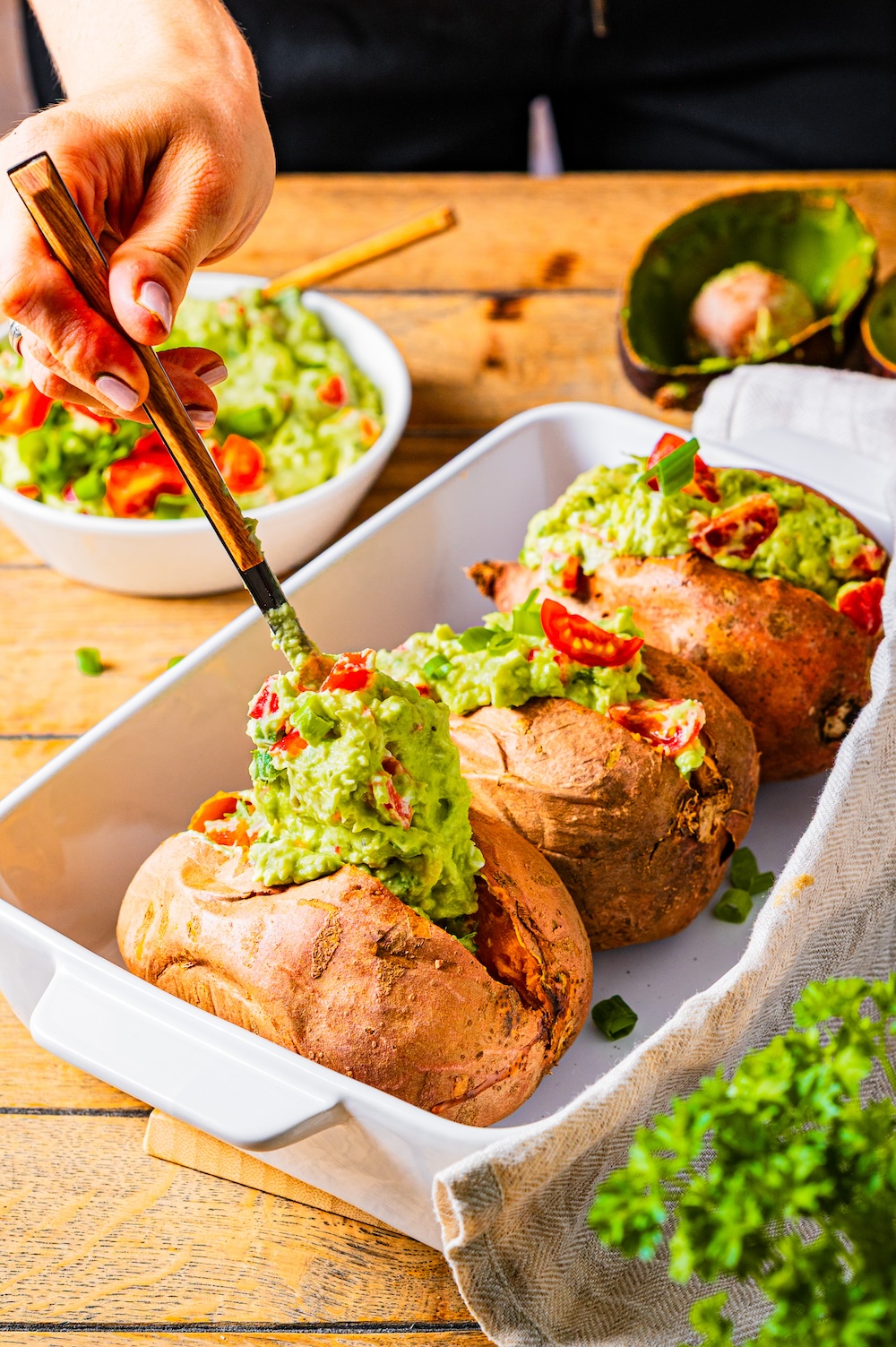 Gebackene Süßkartoffeln werden gerade mit einer Avocado-Creme befüllt.