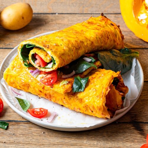 Kürbis-Kartoffel-Rolle, gefüllt mit Tomaten, Spinat und Avocado, in 2 Teile geteilt und auf einem Teller angerichtet.