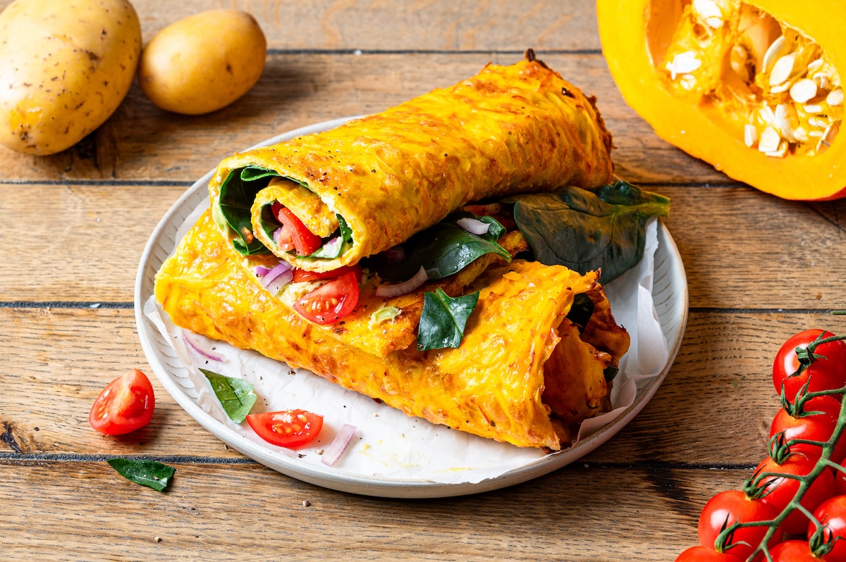 Kürbis-Kartoffel-Rolle, gefüllt mit Tomaten, Spinat und Avocado, in 2 Teile geteilt und auf einem Teller angerichtet.