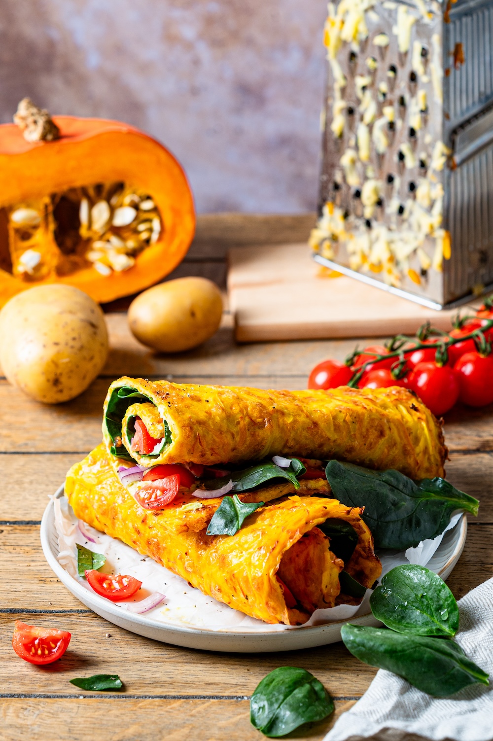 Vegetarische Kürbisrolle mit Spinat, Tomaten und Avocado gefüllt auf einem Teller.