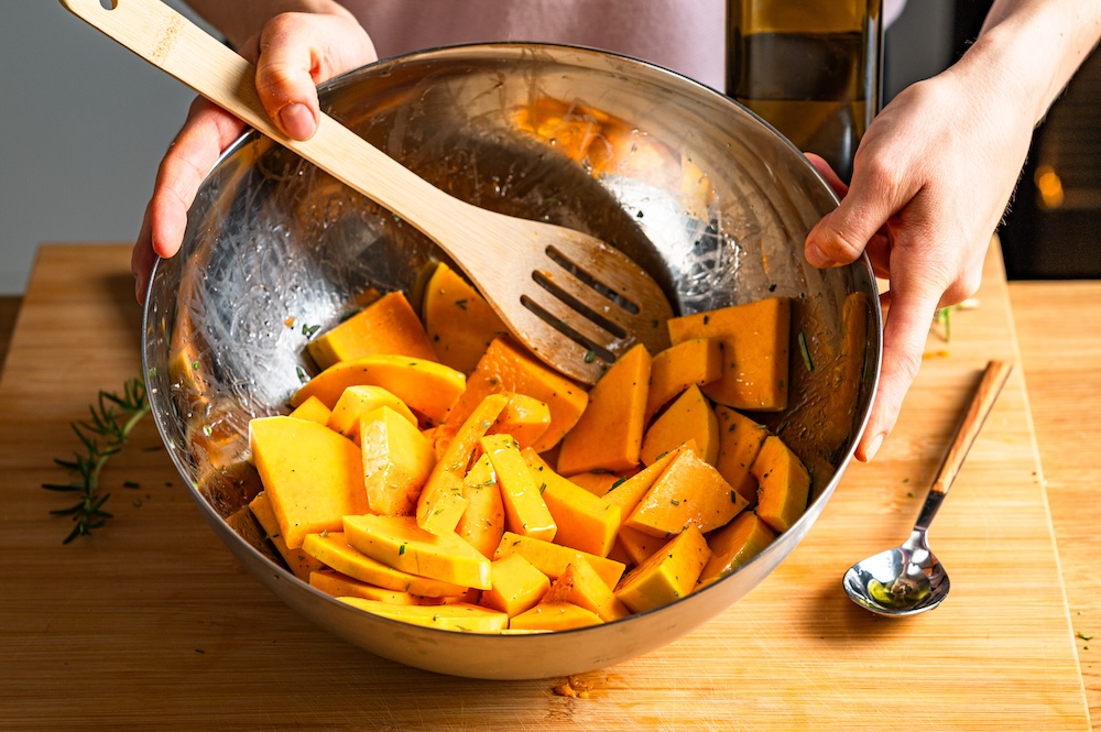 Butternut-Kürbis-Stücke werden in einer Schüssel mit Öl und Rosmarin vermengt.