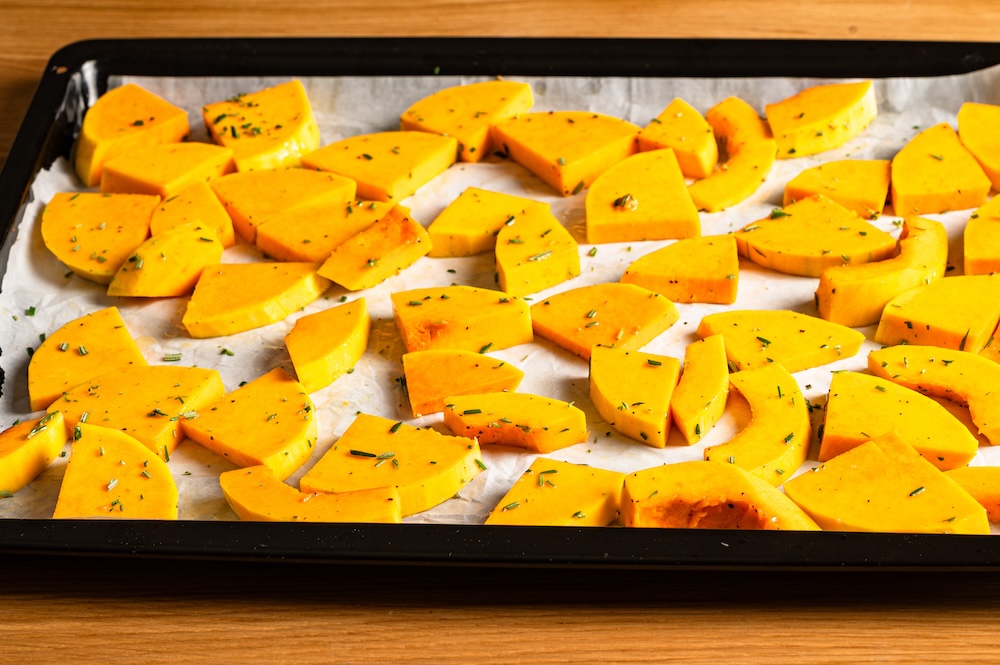 Marinierte Butternut-Stücke auf einem Blech mit Backpapier.