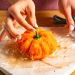 Der Stiel einer grünen Paprika wird auf den Frischkäse-Kürbis gesetzt.