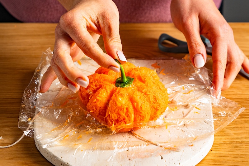 Der Stiel einer grünen Paprika wird auf den Frischkäse-Kürbis gesetzt.