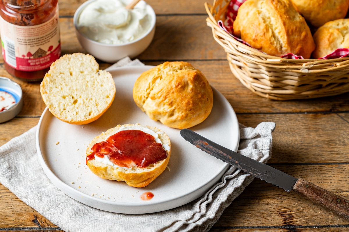 Dinkel-Quark-Brötchen auf einem Teller, eines davon ist aufgeschnitten und mit Marmelade bestrichen.