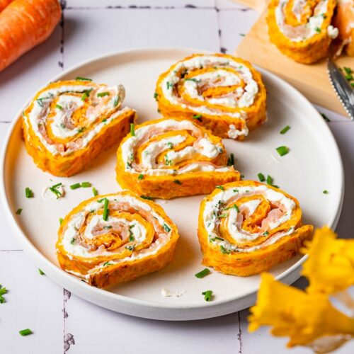 Karotten-Frischkäse-Rolle mit Räucherlachs in Stücken auf einem Teller.