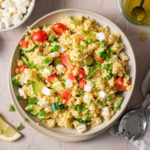 Hirsesalat mit Feta, Gurke, Paprika und Tomaten in einer Schüssel serviert.