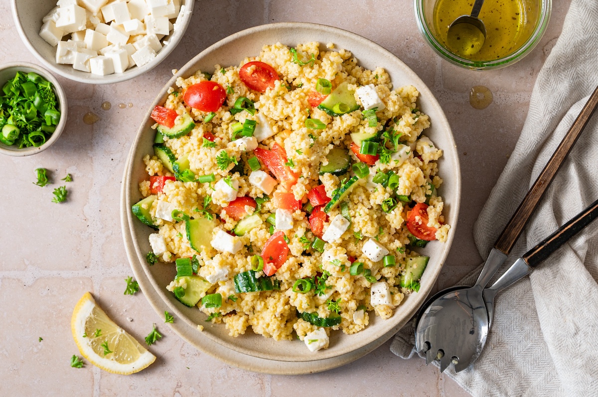Hirsesalat mit Feta, Gurke, Paprika und Tomaten in einer Schüssel serviert.